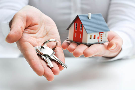 Hands holding a model house and set of keys.