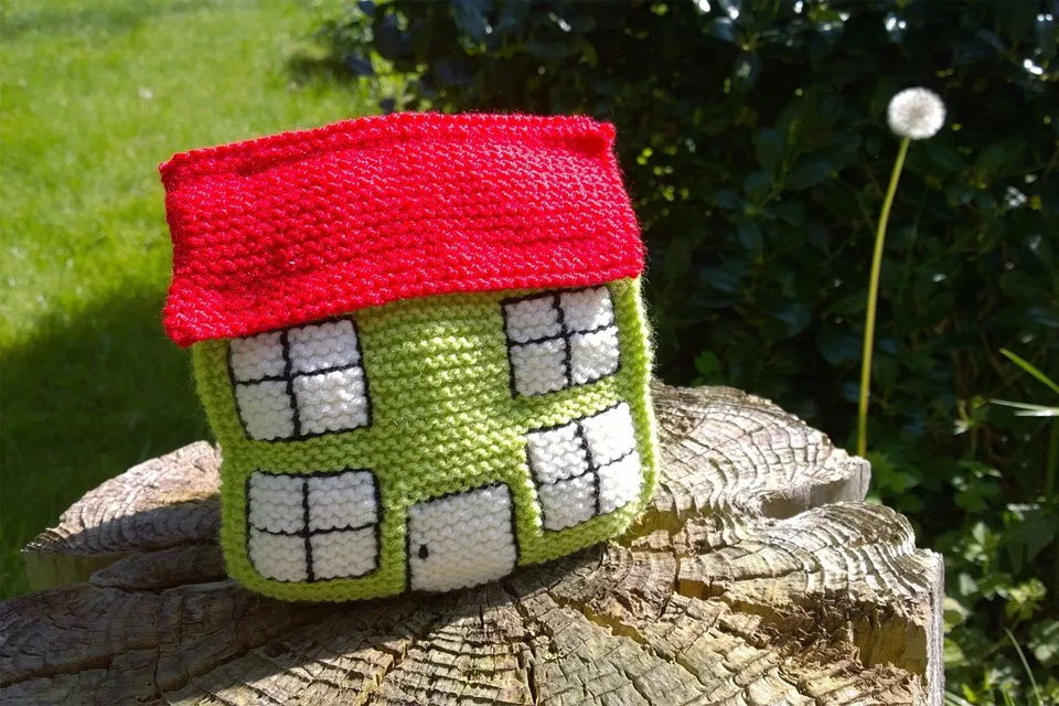 A knitted house sitting on top of a tree stump.