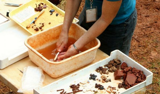 An archaeologist washes an artifact excavated at a dig.