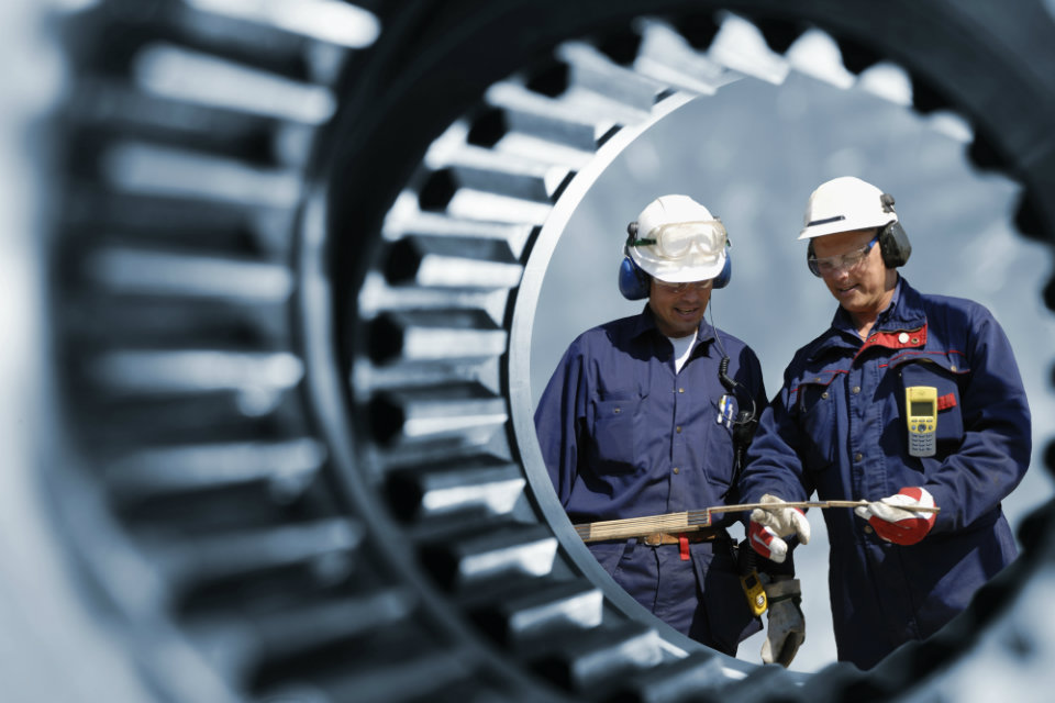 Two engineers at work, viewed through a cog wheel.