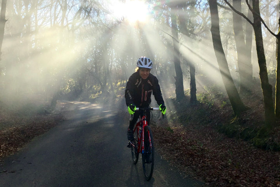 Rachel Jones cycling through woodland, with light shining through trees behind her.