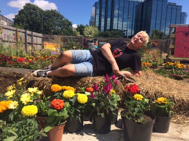 Hannah Cummings lying on a heap of vegetation with potted plans arrayed in front of her.