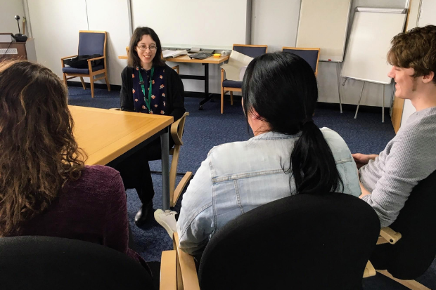 Rebecca sitting next to a table, talking to three colleagues.