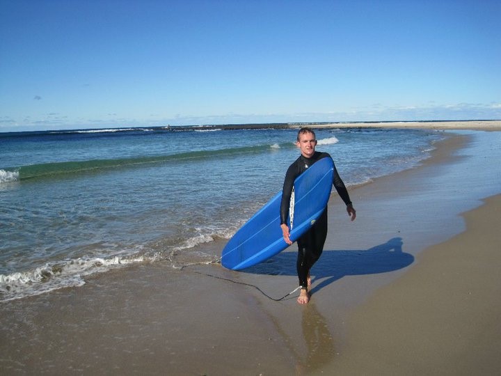 Author Rory Nicholls carrying surfboard on an Australian beach.