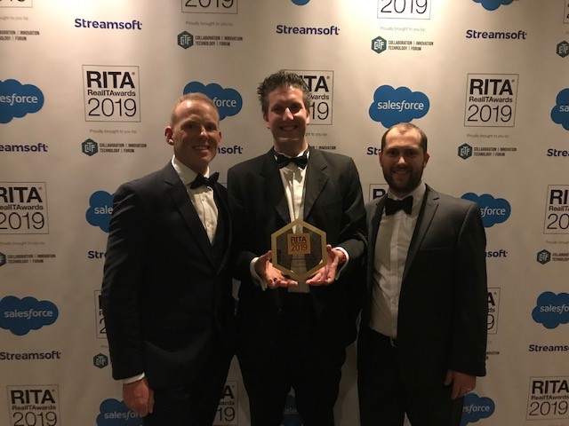 Three men in evening suits holding an award against a background saying 'Real IT Awards 2019'.