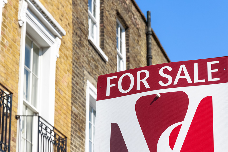 Photo of a 'For sale' sign in front of a terrace of houses.