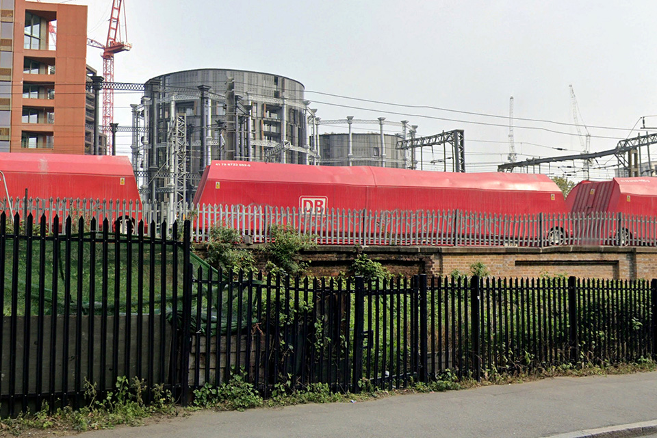 Gas holders converted into homes behind a railway line and a fence.