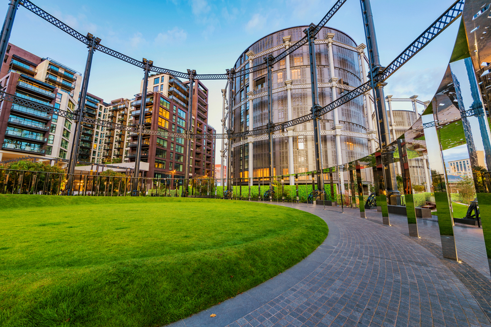 A gasholder converted into homes viewed through the frame of a neighbouring gasholder turned into a park.