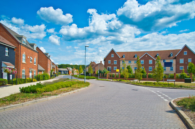 A road junction on a suburban estate with detached homes on the left-hand side and an apartment block ahead.