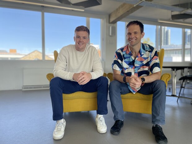 Viability co-founders Henry Mayell and Adria Tarrida sitting side by side in armchairs in an office, smiling and with their hands clasped in front of them.