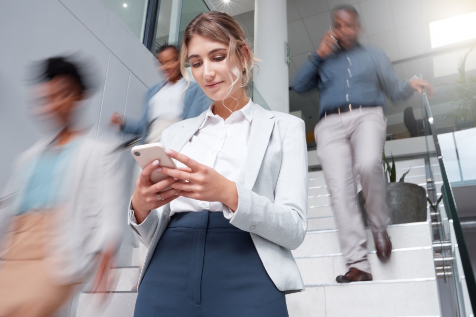 Woman looking at her device as people rush around her at speed.