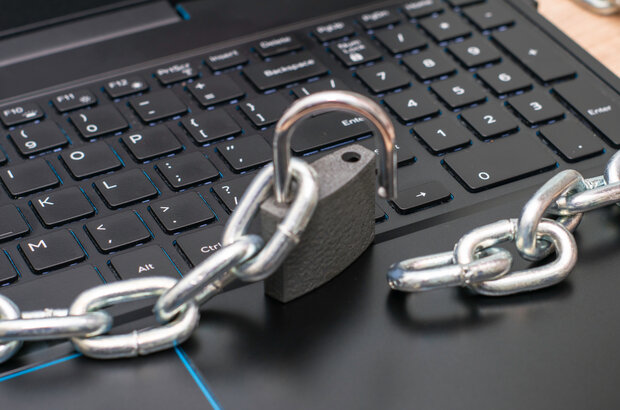 An open padlock sitting on a laptop keyboard, with a chain linked to the padlock on the left but the other end lying flat to the right.